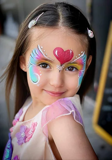 Niña con pintacaras multicolor y un corazón rosa